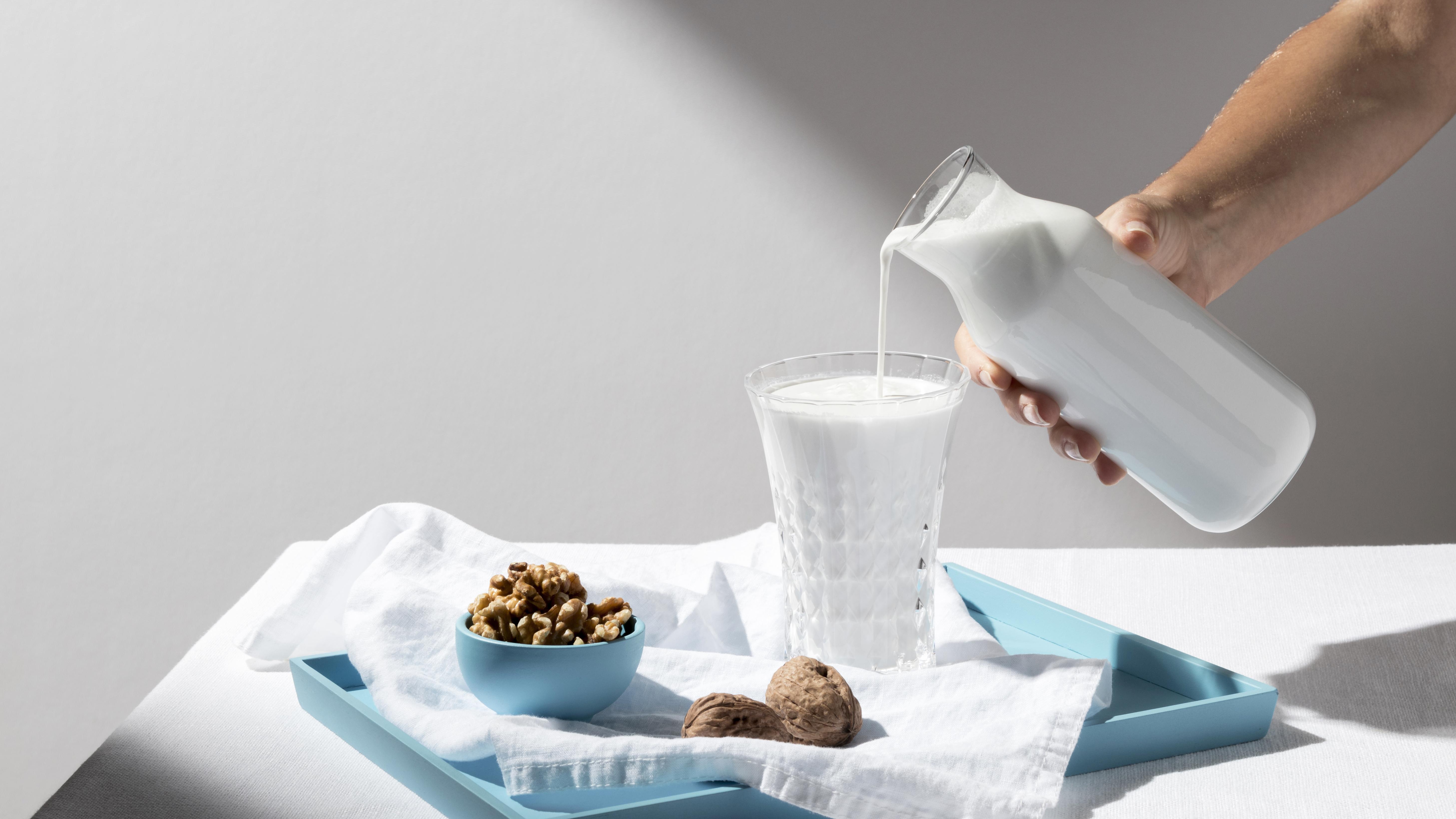 person-pouring-milk-full-glass-with-walnuts-tray.jpg